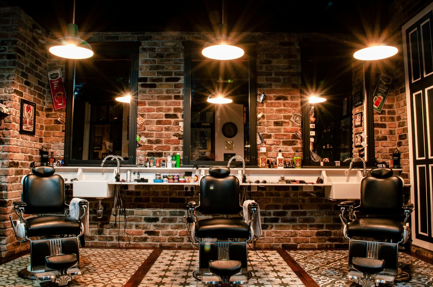 Barbershop s tromi kreslami, tehlovou stenou a závesnými lampami.